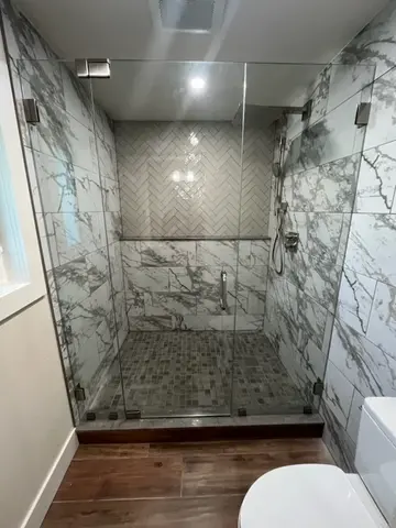 A frameless glass shower door on a marble tiled shower in a full bathroom remodel project by Glass Doctor of Tampa Bay.