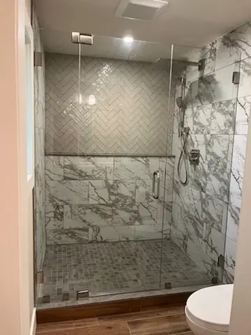 A custom frameless glass shower door installed on a shower with marble tiles as part of a bathroom remodel by Glass Doctor of Pinellas County.