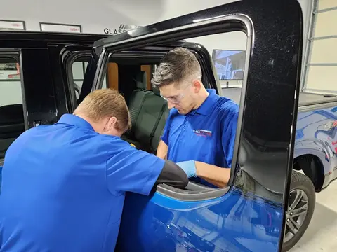 Two service professionals from Glass Doctor Auto of Cedar Park work together to replace a rear door window on a pickup truck.