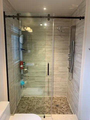 A sliding glass shower door with black hardware installed on a walk-in shower by Glass Doctor of York Region.