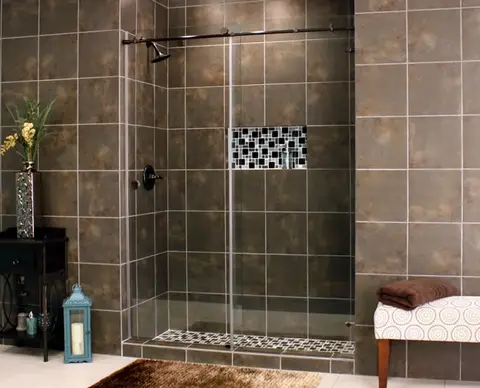 A brown tiled shower with a sliding glass door of two frameless clear glass panels and black hardware.