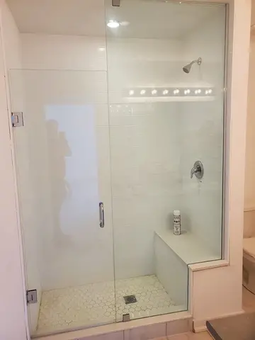 A white tile shower with a seat and straight frameless glass enclosure and swinging door installed by Glass Doctor of Barrie, ON.