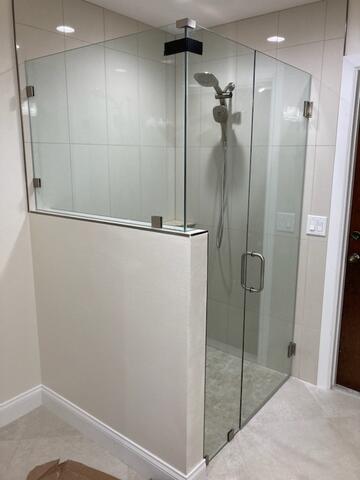 A frameless glass shower enclosure with a half-wall and three panes of glass by Glass Doctor of Sarasota.
