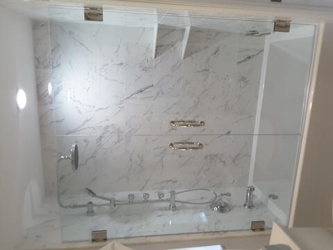 A tub with marbled walls and a frameless glass double-door enclosure and chrome hardware by Glass Doctor of Pinellas County.