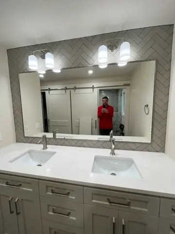 A mirror mounted on a gray tiled wall over a double-sink vanity on a bathroom remodel project by Glass Doctor of Tampa Bay.