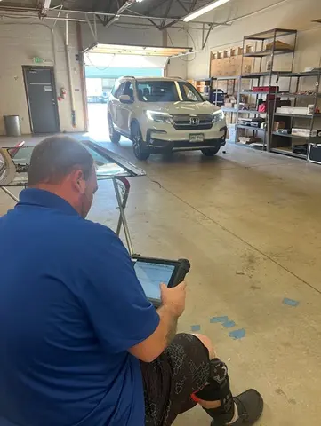 A white SUV in the work bay and a Glass Doctor Auto of Castle Rock service professional in the foreground looking at a tablet.