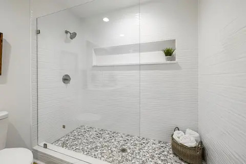 A walk-in shower with white tiles and a frameless clear glass splash panel.