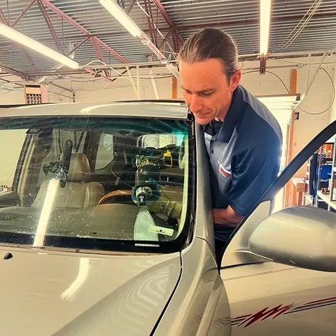 A Glass Doctor Auto of Castle Rock service professional using a tool to remove the windshield of a silver vehicle.