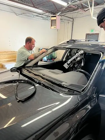 Two Glass Doctor Auto of Castle Rock service professionals working on a windshield replacement on a dark gray vehicle.