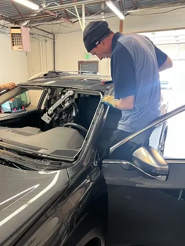 A Glass Doctor Auto of Castle Rock service professional standing in the door of a vehicle and working on a windshield replacement.