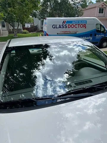 A white car with a newly installed windshield and the Glass Doctor Auto of Castle Rock mobile service van in the background.