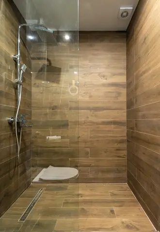 A shower with wood-grained tile and a clear glass splash panel.