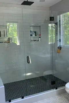 A glass shower enclosure with two frameless fixed panels and a swinging door in the middle on a white-tiled shower by Glass Doctor of Nashville.