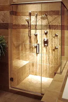 A beige shower with a 2-sided glass enclosure, a swinging door, and a bronze top frame.