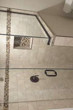 A beige tiled shower with a half wall on one side and a custom frameless glass shower enclosure from Glass Doctor of Sarasota.