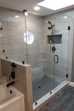 A gray tile shower with frameless glass at 90-degrees, a swinging door, and dark hardware by Glass Doctor of Raleigh