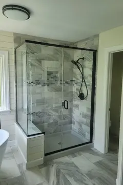 Semi-frameless glass shower with black hardware and a swinging door on gray tiles by Glass Doctor of Raleigh