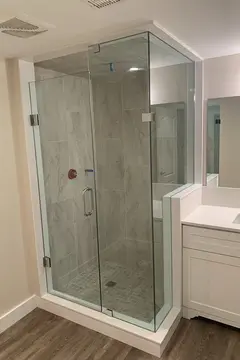A grey tiled walk-in shower with a 90-degree frameless glass enclosure and chrome hardware by Glass Doctor of Newmarket.