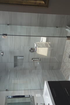 A gray tiled shower with a 90-degree frameless glass enclosure and chrome hardware installed by Glass Doctor of Pinellas County.