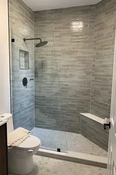 A shower with gray tiles and a frameless glass splash panel cut at an angle and installed by Glass Doctor of Nashville.