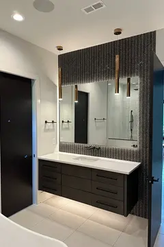 A mirror with back-lighting on a black tiled wall above a white countertop installed by Glass Doctor of Nashville.