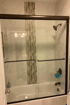 Sliding glass shower doors with a bronze frame and hardware installed on a tub by Glass Doctor of Ocala.
