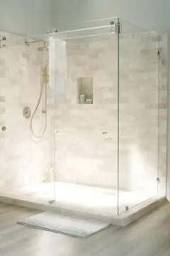 A beige corner shower with a two-sided frameless clear glass enclosure and a swinging door.