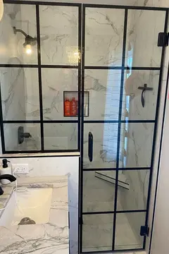 Two black-framed glass panels installed on a white marble shower enclosure by Glass Doctor of Nashville.