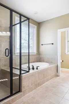 A large bathroom with a shower enclosed in clear glass and black metal frame.