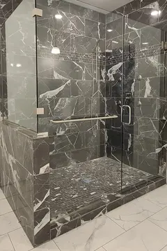 A shower with black and white marbled tiles and a frameless clear glass enclosure with swinging door.