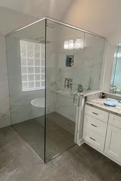 Frameless glass shower with swinging door and a chrome header and hinges on a white and gray tile shower