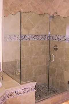 A clear frameless glass shower enclosure with a wavy decorative top edge on a light brown tiled shower.