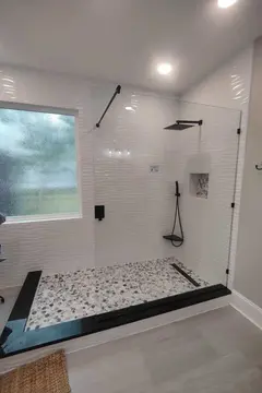 A shower with white textured tile and a frameless clear glass splash panel with black hardware by Glass Doctor Home + Business of Myrtle Beach.