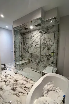 A custom shower enclosure featuring frameless glass panels surrounding marble tiles and benches on each side installed by Glass Doctor of Newmarket.