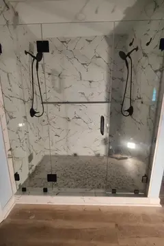 A three frameless glass panel shower enclosure with black hardware on a white marble shower installed by Glass Doctor Home + Business of Myrtle Beach.