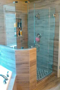 A tan tiled shower with an angled half-wall on one side topped with frameless glass splash panels and a full-height frameless glass door by Glass Doctor of Nashville.