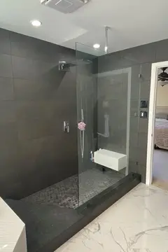 An open shower with dark gray tile and a frameless glass splash panel and chrome ceiling mount by Glass Doctor of Raleigh