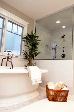 A shower in a white bathroom with slightly tinted frameless glass panels and black hardware.