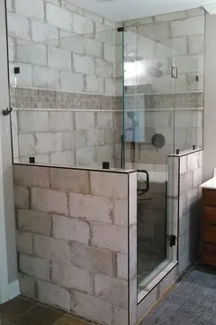 A shower enclosure with two half-walls topped with frameless glass splash panels and a frameless glass door between them by Glass Doctor of Nashville.