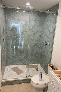 A sliding frameless glass door installed by Glass Doctor of Nashville on a shower with tiles that look like fish scales.
