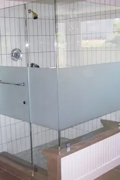 A frameless shower enclosure with a strip of sandblasted glass across the middle on a white tile shower.