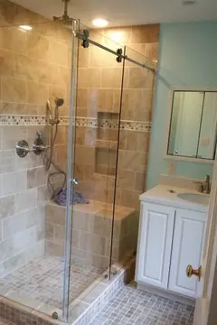 A brown tiled shower with a 90-degree frameless glass enclosure and sliding door.