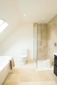 A beige tile shower in a white bathroom with a frameless clear splash panel.