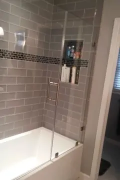 Frameless glass panels and swinging door installed on a white tub with dark gray tiles.