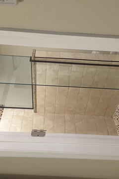 Frameless glass splash panels installed by Glass Doctor of Pinellas County on an open shower stall with tan tiles.