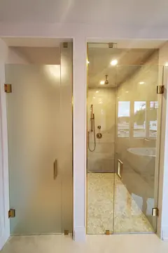 Two side-by-side glass shower door installations, one clear and one frosted, with swinging doors and gold hardware by Glass Doctor of Muskoka.