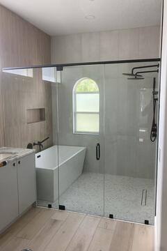 A wet room bathroom with a tub and shower behind a semi-frameless straight glass enclosure with black hardware by Glass Doctor of Sarasota.