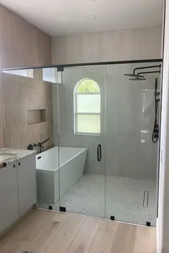 Custom glass with a center door and black hardware on a wet room with tub and shower installed by Glass Doctor of Tampa Bay