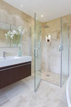 A frameless shower enclosure with clear glass and a 90-degree angle in a beige tile bathroom.