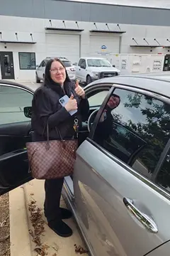 A satisfied customer of Glass Doctor Auto of Cedar Park gives two thumbs up in front of her silver car.